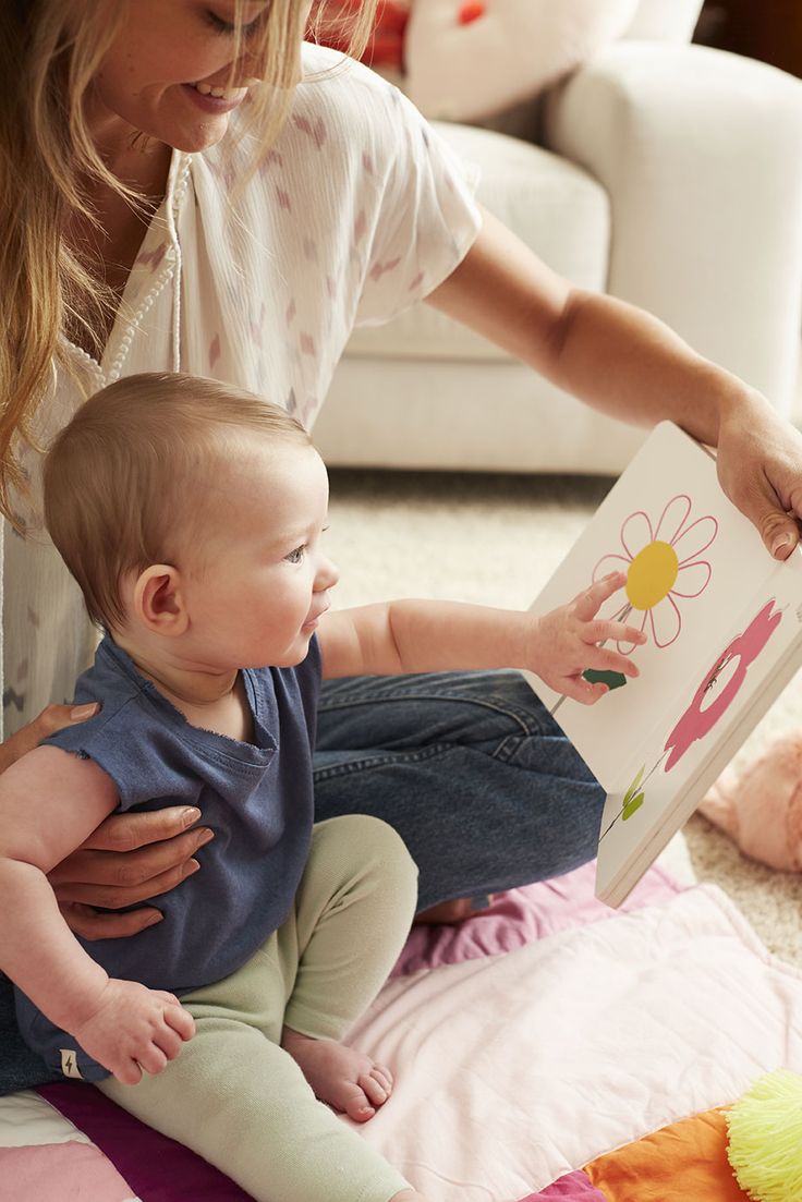 This may contain: a woman is holding a baby with a book in her lap while sitting on the floor