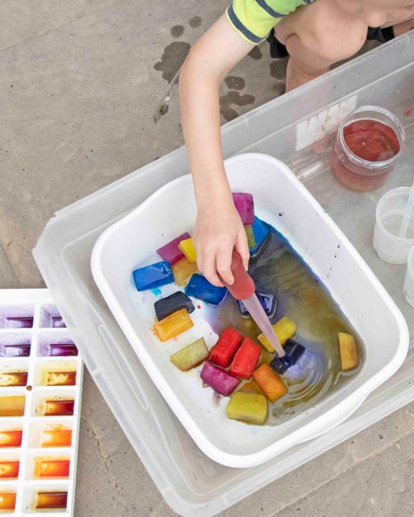 A child squeezes water onto colored ice cubes.
