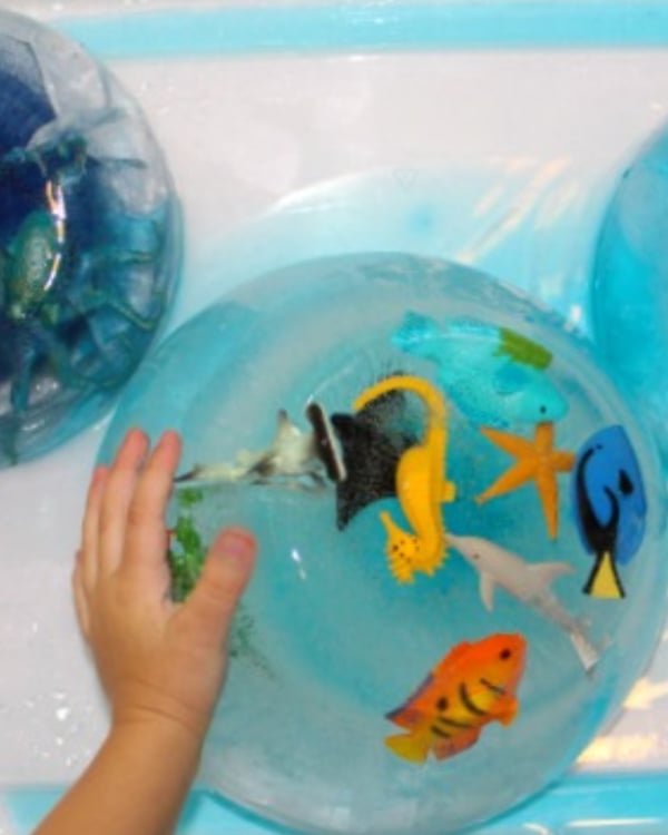 A child's hand touches a frozen bowl of water and toys.