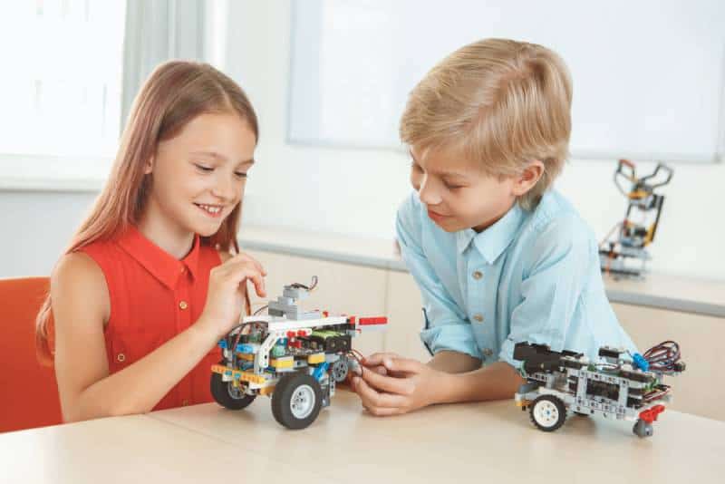 brother and sister having robotics class sitting at table making robots smiling cheerful
