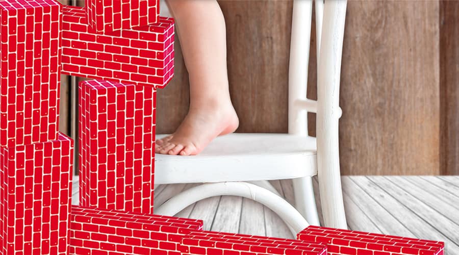 young toddler standing on a chair stacking giant blocks building her gross motor skills