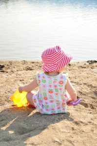 baby sitting on a sandy beach with a bucket and shovel in hand
