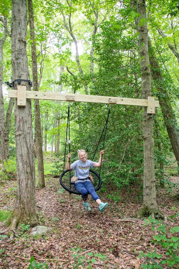 This may contain: a woman sitting on a swing in the woods