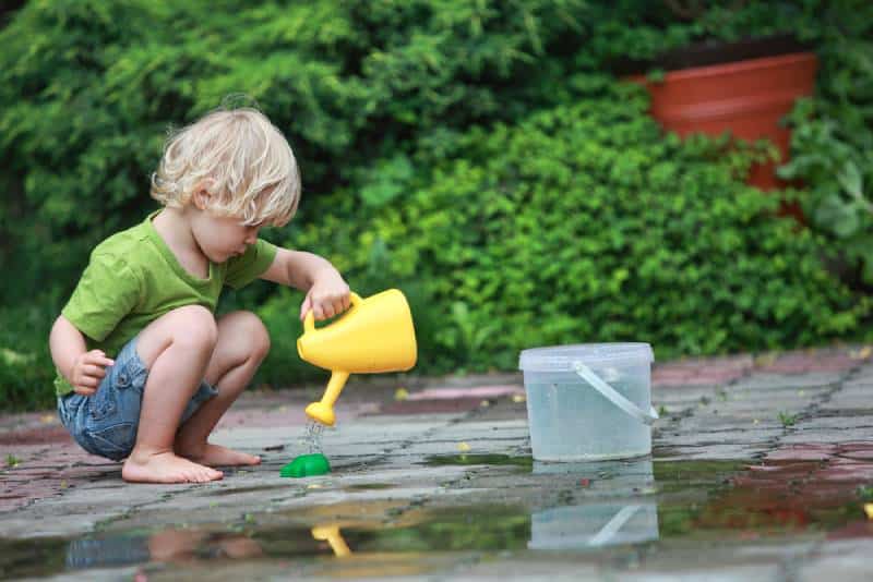 White little barefoot girl playing with water outdoors