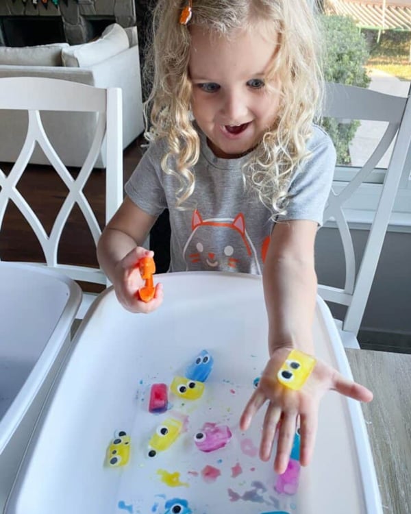 A child looks down excitedly at a yellow ice cube with eye balls.