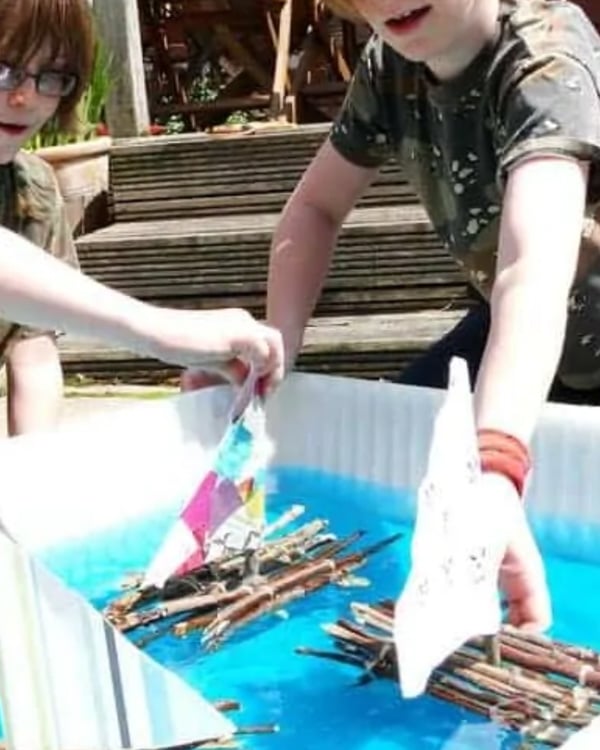 Two children play with stick rafts on water.