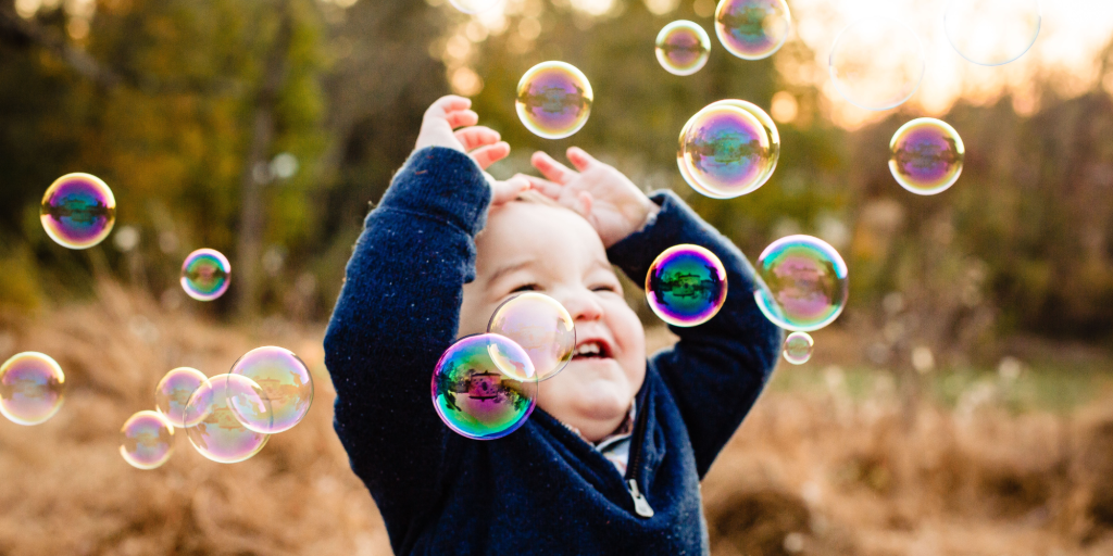 A young child is outside playing in bubbles that float through the air.