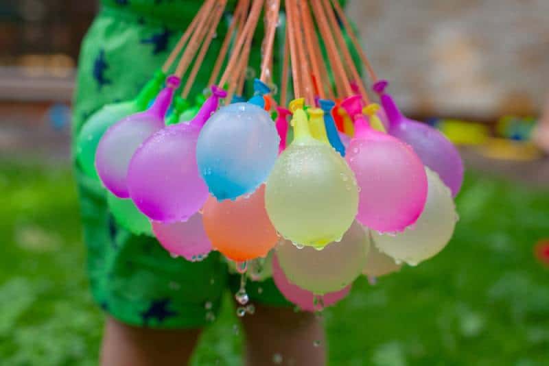 Kid holds filled water baloons are ready to be played with in garden