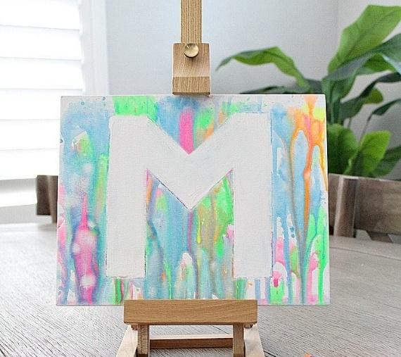 a canvas sitting on an easel covered in paint that was shot from a water gun and four different colored water guns are laying on the table in front of the canvas