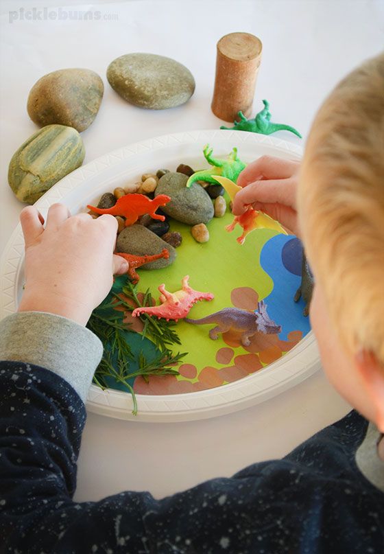 This may contain: a young boy is playing with rocks and paper plate dinosaurs on a table next to some stones
