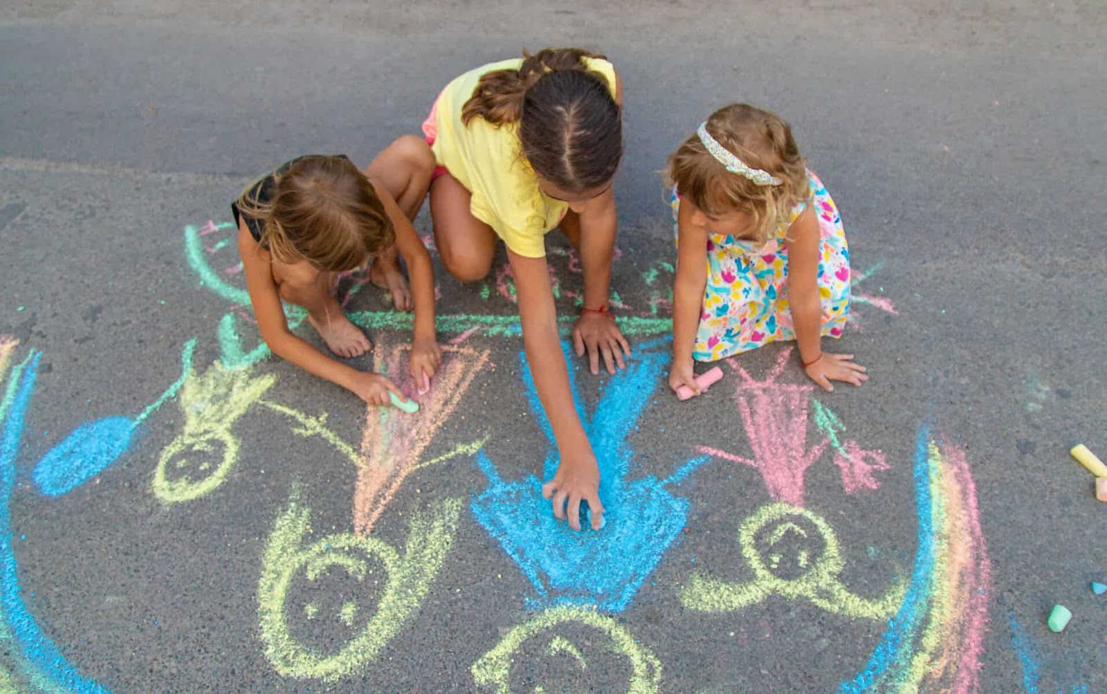 three young girls creating sidewalk chalk self portraits