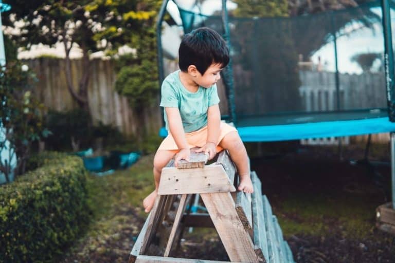 A toddler playing in the backyard climbing a wood structure.