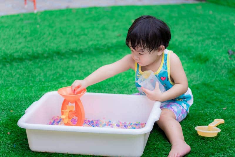 boy is playing colorful water beads in white basin in his garden