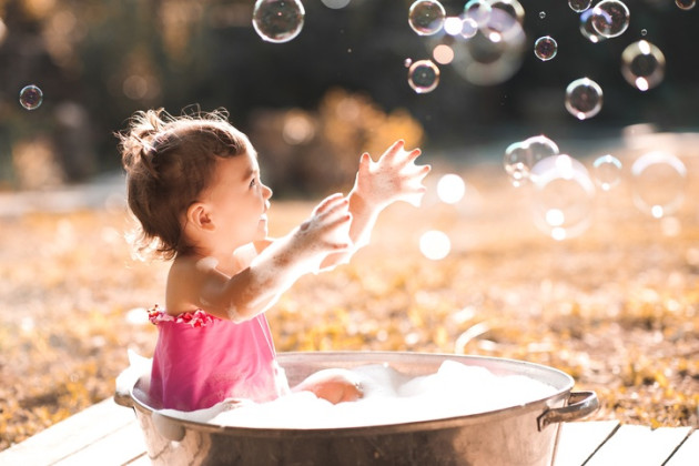 Laughing baby girl playing with soap bubbles outdoors.