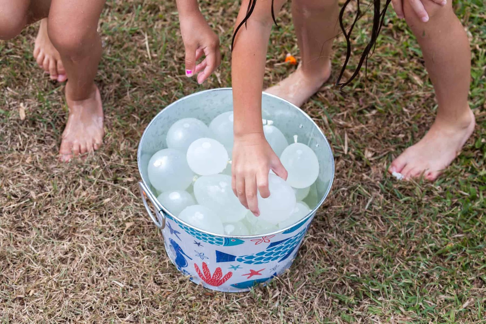 kids reaching into a bucket of filled water balloon getting ready for water balloon games 