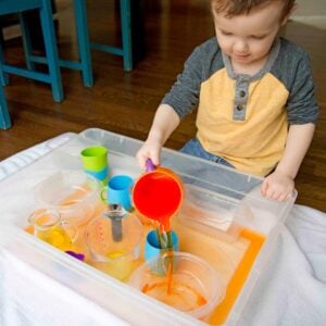 A toddler pours orange water into a plastic container.