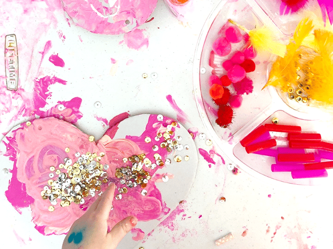 Child adding sequins to painted cardboard heart