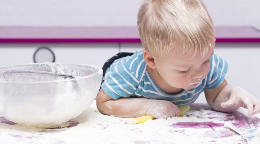 little boy engaged in exploratory play on a purple kitchen counter covered in spilled flour