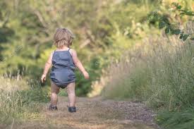 Baby girl walks away on green forest ...